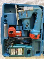 Makita cordless jigsaw, battery charger, extra battery, all secured inside the blue molded plastic carrying case