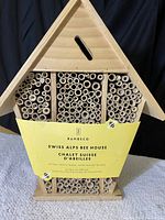 Front view of the wooden bee house shaped like a chalet with bamboo tubes and yellow Bambeco product label promoting bee population support.