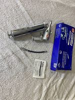 Full kit laid out showing the pneumatic grease gun, flexible hose, instruction manual, and original box on a carpeted surface.