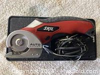 Top view of the red and black SKIL electric cutter with circular blade and power cord coiled beside it inside black carrying case.