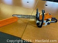 Full view of Stihl chainsaw with guide bar, chain, and orange plastic scabbard on tabletop