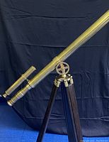 Side view of the lacquered brass telescope mounted on the wooden tripod stand against a black backdrop.