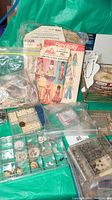 Mixed lot of sewing pattern, beads, and jewelry findings displayed on blue cloth, showing pattern envelope and plastic organizers with beads and jewelry parts.