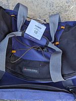 Close-up photo showing the High Sierra brand logo on the navy and black rolling duffel bag with gray straps.