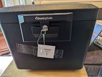 Front view of black Sentry Safe with key lock and two attached keys.