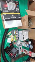 Photo showing LED flood light bulbs packaging, assorted electrical parts, pegboard pegs, screws, and a few spray cans and tools arranged on a green surface.