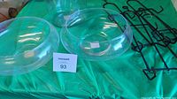 Covered glass jar, two glass bowls, and four metal plate hangers on green fabric surface