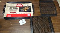 Grill topper with label showing Expert Grill brand and dimensions plus two charcoal broil baskets side by side on a wooden table.
