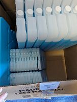 Box containing multiple blue and white ice packs stacked upright and flat along with silicone ice trays.