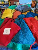 Photo showing five sweaters in various colors (yellow, orange, red, bright blue, royal blue) and one denim skirt folded on top. Sweaters appear plus size L-XL, skirt size 18.