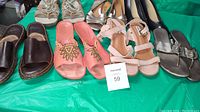 Full view of seven pairs of mixed style ladies shoes arranged on green surface showing variety of styles and colors including brown leather, pink suede, metallic and black pumps.