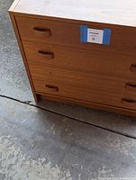 Close-up front view of medium finish pressboard nightstand's drawers and handles with missing handle at top right.