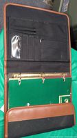 Open brown leather office folio showing card slots, clear ID window, and ring binder with green photo paper inside