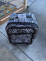 Front view of Kathy Van Zeeland rolling carry-on bag with black and white zebra print and visible brand plaque.
