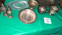 Full view of silver and silver-plated items on green table.