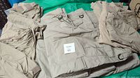 Four pairs of tan tactical pants with multiple pockets and belt loops, folded and laid out