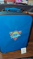 Front view of a blue softside suitcase with 'World Class Traveler' logo, wheeled, showing vintage style and condition with some wear.