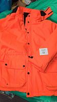 Front view of bright orange shell jacket with snap button closure and front pockets.