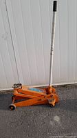 Side view of the orange hydraulic floor jack with handle upright showing its overall condition and wheels.