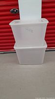 Two stacked translucent plastic storage bins with fitted lids, branded Gracious Living, near a red storage unit door.