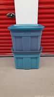 Two stacked blue Rubbermaid Roughneck tote bins with lids, showing front view and condition.