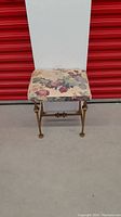 Front view of antique brass foot stool with floral cushioned top showing overall structure and condition.