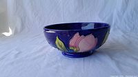 Side view of blue ceramic bowl with hand painted pink flowers and green leaves, showing the pedestal base and bowl shape.