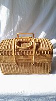 Front view of classic wicker picnic basket with rectangular shape and curved wicker handle.
