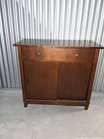Front view of the large MCM style side table showing drawer with two metal pulls and sliding doors below.