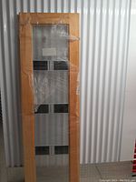 Front view of the Milette glass and wood door wrapped in plastic, showing the wood frame and decorative glass panel.