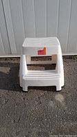 Front view of white plastic Mistral Ultra Safe Step Stool with two non-slip steps and red label on top step.