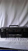 Front view of Panasonic RX-CW26 portable stereo boombox showing handle, antenna, speakers, and front control panel with cassette decks and radio tuner.
