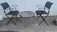 Full set showing one round metal mesh top table and two black metal frame chairs with black mesh fabric seats and backs.