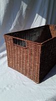 Rectangular wicker basket angled to show front and one side, with a cut-out handle visible on the side.