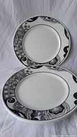 Photo showing 2 of the Corelle dinner plates, one round and one oval, with black and gray floral and abstract pattern on rims, white center.