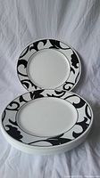 Stack of 8 round Corelle dinner plates showing black and white floral rim design on the top plate.