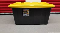 Front view of the large Sterilite tote bin with yellow lid and black base.