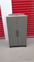 Full front view of green storage cabinet with two doors on caster wheels in front of red door.