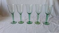Full set of 5 green wine goblets shown side-by-side on white cloth background.