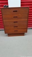 Front view of vintage wooden dresser showing five drawers with rectangular inset handles and warm brown wood finish.