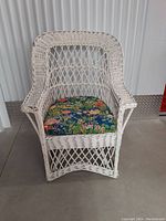 Front view of white painted wicker armchair with floral cushion showing woven lattice design and chair shape