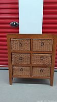 Front view of wooden shelving unit with six wicker drawers and metal ring pulls.