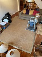 Full view of tan woven area rug laid out in a room with a sofa and other household items around it.