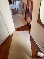 Two white area rugs laid on hardwood floor in hallway, showing texture and wear.