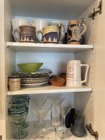 Photo showing shelves with various ceramic mugs, decorative beer steins, ceramic bowls, plates, cocktail glasses, and shot glasses arranged for inventory.