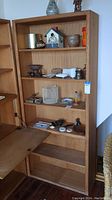 Wood bookcase standing upright with five shelves, three adjustable. Various household items on shelves in photo but not included in sale.