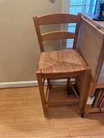 Single wooden chair with woven wicker seat, natural wood finish, shown against a wall and hardwood floor.