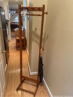 Full view of wooden coat rack showing base, vertical structure, hooks, mirror, and umbrella holder with umbrella.