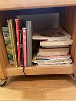 Bookshelf section containing multiple worn cookbooks and recipe binders stacked and lined up