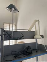 Photo showing three desk lamps together on a surface: green lamp with metal rods, cream articulated lamp, black lamp with curved arm